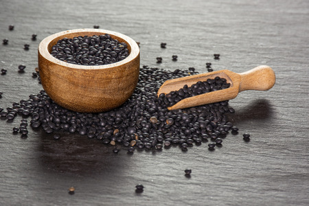 Set lot of whole black lentils beluga variety with wooden bowl on grey stoneの写真素材