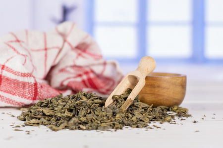 Lot of pieces of dry green tea tea towel with wooden scoop with blue windowの写真素材