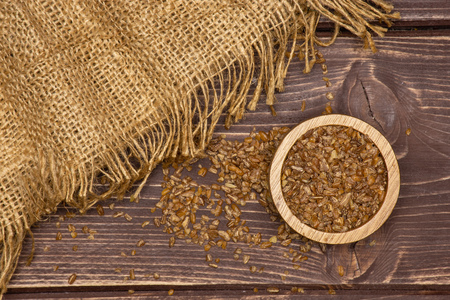 Lot of whole raw bulgur grains with wooden bowl flatlay on brown woodの写真素材