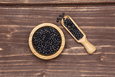 Lot of whole black lentils beluga variety scoop with wooden bowl flatlay on brown woodの写真素材
