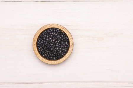 Lot of whole black lentils beluga variety with wooden bowl flatlay on white woodの写真素材