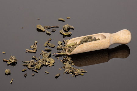 Lot of pieces of dry green tea with wooden scoop on black glassの写真素材