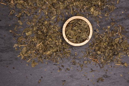 Lot of pieces of dry green tea with wooden bowl flatlay on grey stone