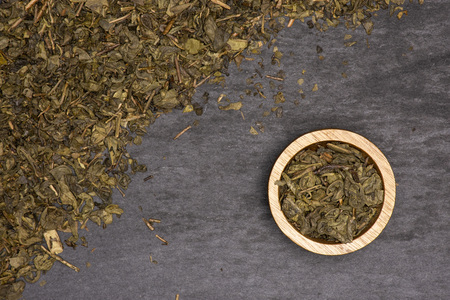 Lot of pieces of dry green tea with wooden bowl flatlay on grey stoneの写真素材