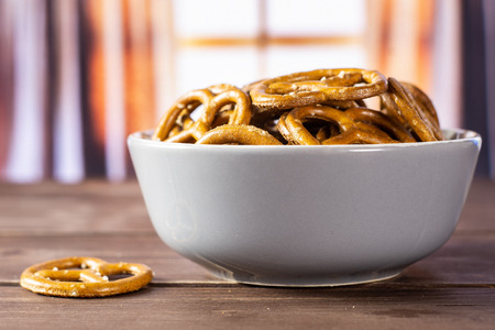 Lot of whole mini salted pretzels in a grey ceramic bowl with silk curtainsの写真素材