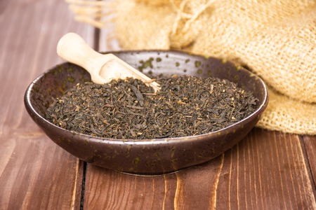 Lot of pieces of dry black tea earl grey in a grey ceramic bowl with wooden scoop on jute cloth on...