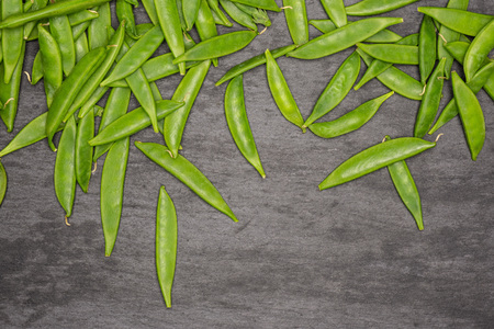 Lot of whole green sugar snap pea pods flatlay on grey stone
