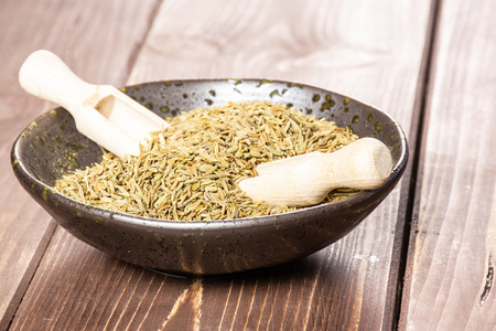 Lot of whole roman caraway seeds two wooden scoops in a grey ceramic bowl on brown woodの写真素材