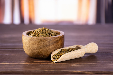 Lot of whole roman caraway seeds with wooden bowl with silk curtains behindの写真素材