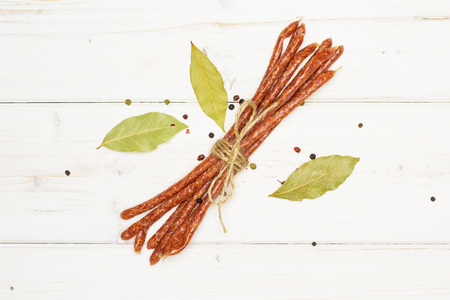 Lot of whole spicy salami stick tyrolini tied by jute with black pepper and bay leaf flatlay on...