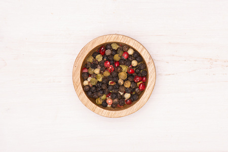 Lot of whole peppercorns of four colors with wooden bowl flatlay on white wood