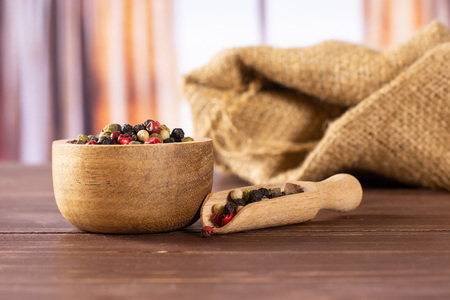 Lot of whole peppercorns of four colors with wooden bowl on jute cloth with wooden scoop with silk...