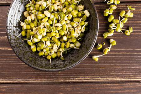 Lot of whole fresh green bean sprouts mungo in a grey ceramic bowl flatlay on brown woodの写真素材