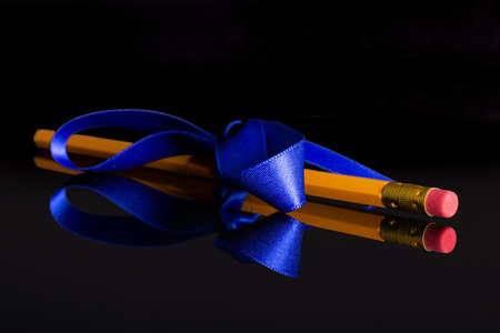 One whole yellow pencil tied by ribbon isolated on black glassの写真素材