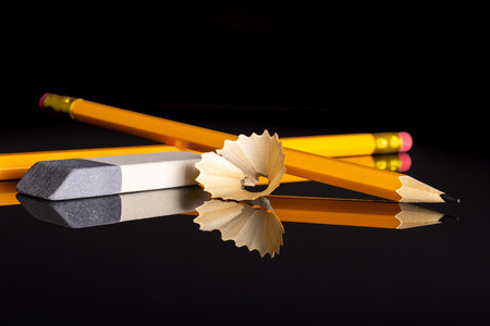 Group of two whole yellow pencil fan-shaped shaving with an eraser isolated on black glass