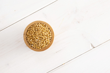 Lot of whole white mustard seeds with wooden bowl copyspace flatlay on white woodの写真素材