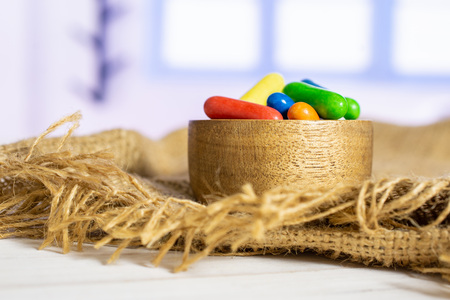 Lot of whole sweet licorice comfit on jute cloth in a wooden bowl with blue window in background