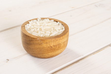 Lot of whole white jasmine rice grains in a wooden bowl on white woodの写真素材