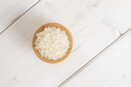 Lot of whole white jasmine rice grains copyspace in a wooden bowl flatlay on white woodの写真素材