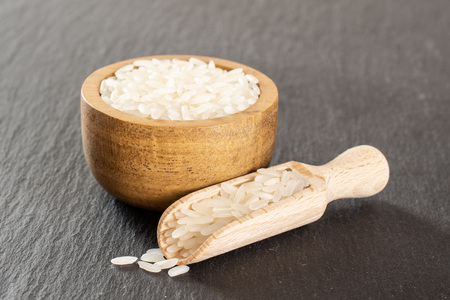 Lot of whole white jasmine rice grains in a wooden bowl with wooden scoop on grey stoneの写真素材