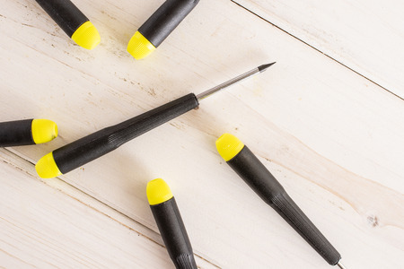 Lot of whole screwdrivers with a yellow black plastic handle work item flatlay on white wood