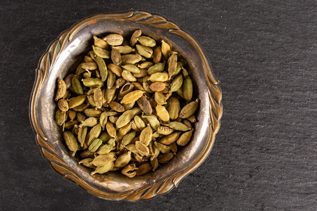 Lot of whole true cardamom pod in old iron bowl flatlay on grey stoneの写真素材