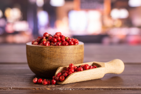 Lot of whole peruvian pink pepper in a wooden bowl with wooden scoop in a restaurantの写真素材
