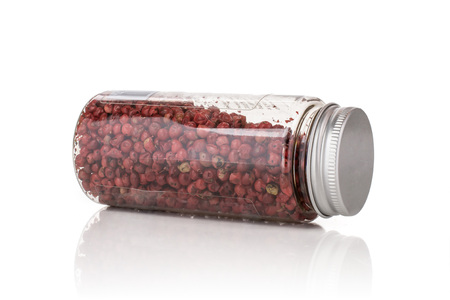 Lot of whole peruvian pink pepper lying on its side in a plastic bottle isolated on white backgroundの写真素材