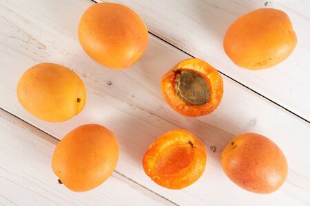 Group of five whole two halves of fresh deep orange apricot with a stone flatlay on white wood
