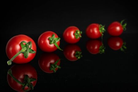 Group of five whole fresh red tomato cherry isolated on black glassの写真素材