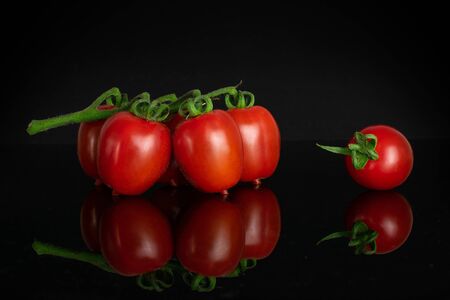 Group of five whole fresh red tomato cherry isolated on black glassの写真素材