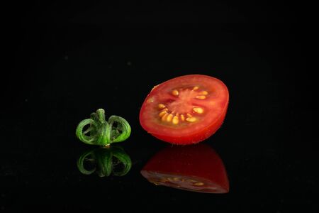 Group of one half one piece of fresh red tomato cherry isolated on black glassの写真素材