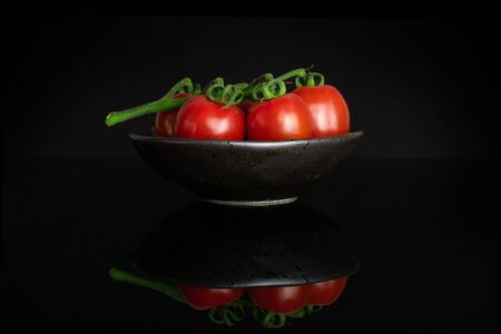 Group of three whole fresh red tomato cherry on a ceramic grey plate isolated on black glassの写真素材