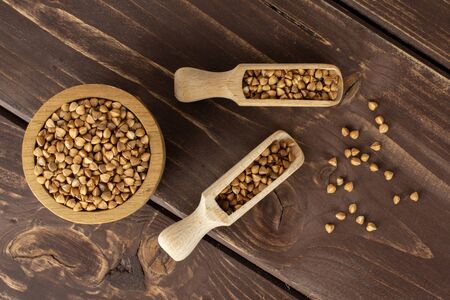 Lot of whole raw brown buckwheat grain in a wooden bowl with wooden scoop flatlay on brown woodの写真素材