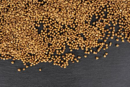 Lot of whole raw brown buckwheat grain copyspace flatlay on grey stoneの写真素材