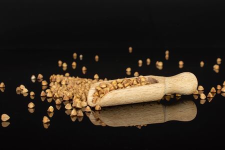 Lot of whole hulled raw brown buckwheat grain with wooden scoop isolated on black glassの写真素材