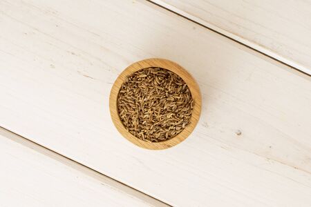 Lot of whole dry caraway fruits in a wooden bowl flatlay on white woodの写真素材