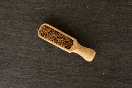 Lot of whole dry caraway fruits closeup with wooden scoop flatlay on grey stone