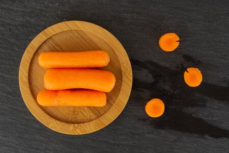 Group of three whole three pieces of peeled orange baby cut carrot on bamboo plate flatlay on grey stoneの写真素材