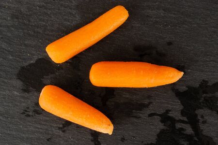 Group of three whole peeled orange baby cut carrot flatlay on grey stoneの写真素材