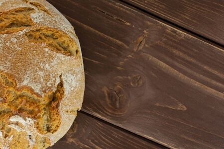 One whole fresh baked rye wheat bread copyspace on right flatlay on brown wood