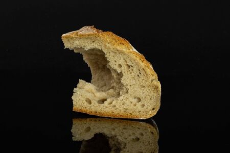 One pinched off fresh baked rye wheat bread slice isolated on black glass