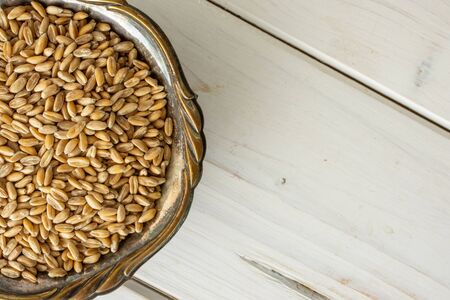 Lot of whole fresh beige dinkel wheat grain in old iron bowl flatlay on white woodの写真素材