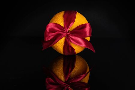 One whole fresh sweet orange with a red bow isolated on black glassの写真素材