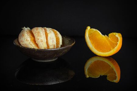Group of one slice four pieces of fresh sweet orange in a dark ceramic bowl isolated on black glassの写真素材