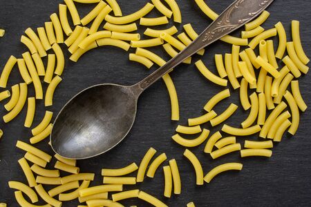 Lot of whole raw pasta macaroni and old iron spoon flatlay on grey stoneの写真素材