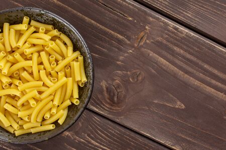 Lot of whole raw pasta macaroni copyspace on right on grey ceramic plate flatlay on brown woodの写真素材