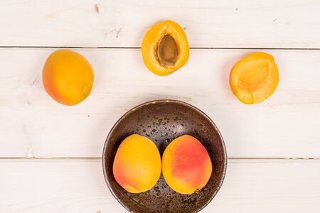 Group of three whole two halves of fresh orange apricot with an apricot stone in a dark ceramic bowl...