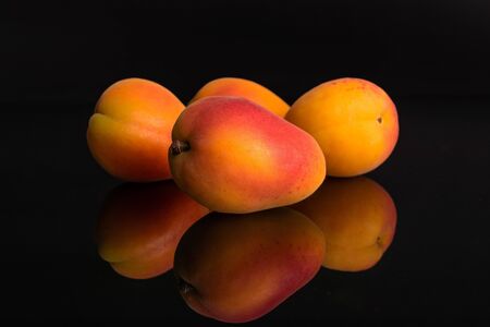 Group of four whole fresh orange apricot one is in the front isolated on black glassの写真素材