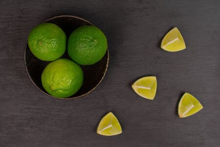 Group of three whole four pieces of fresh green lime in a dark ceramic bowl flatlay on grey stoneの写真素材